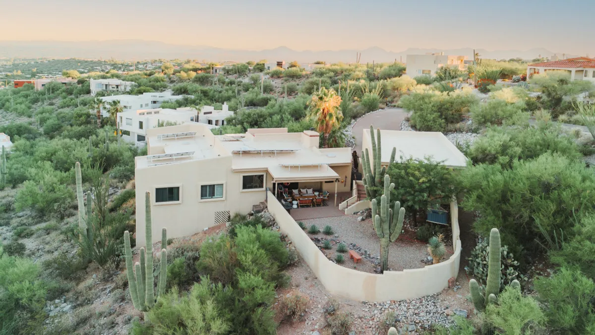 A wide view of the home’s exterior shows Casa Saguaro nestled within a classic desert landscape, surrounded by cacti and native vegetation. There is an inviting outdoor seating area on the private patio, perfect for relaxing with pets or watching them play safely in the enclosed space.