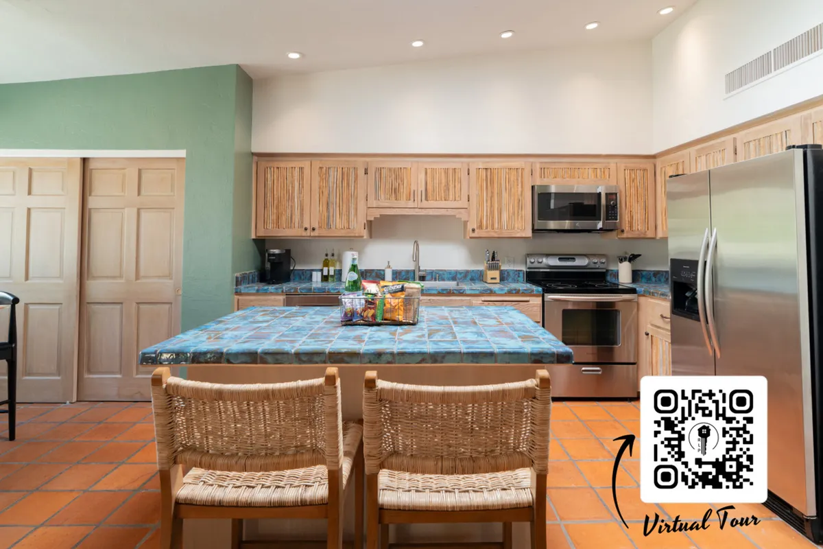 This image features a kitchen with blue tiled countertops, wood cabinetry, stainless steel appliances, and bar stools along the counter. The space appears inviting and practical, suited for both cooking and casual dining or entertaining.
