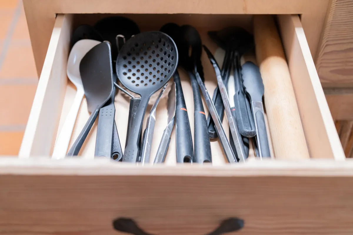 Close-up view of a countertop with an array of kitchen utensils including a rolling pin, spatulas, tongs, and ladles, suggesting readiness for cooking and meal preparation. The setting has a practical and inviting feel.