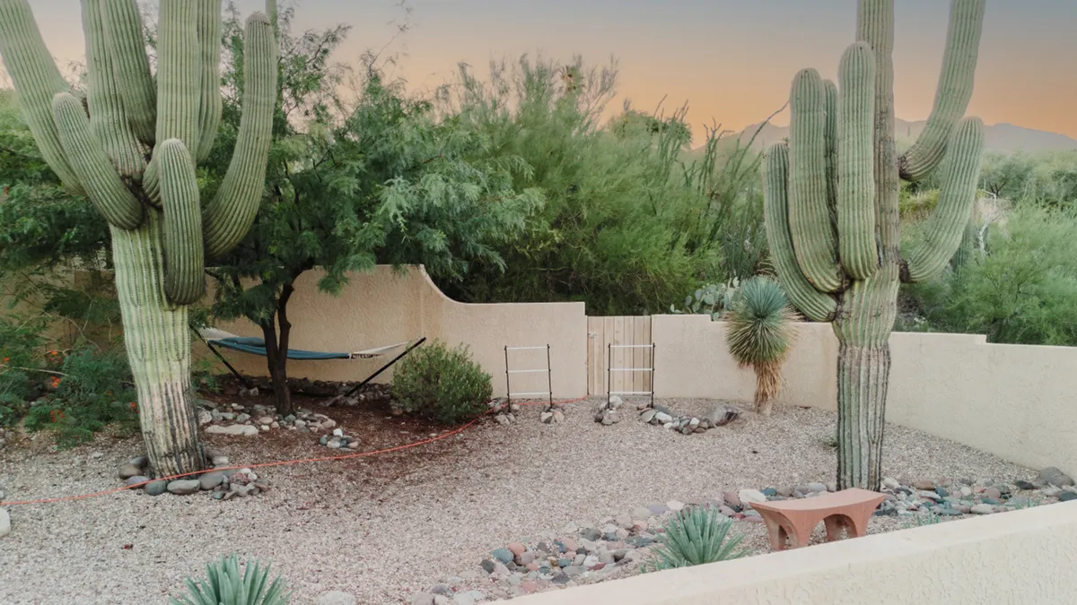 A hammock is strung between tall cacti in a rock garden, with a rustic bench nearby. The scene is sun-drenched and peaceful, inviting moments of relaxation in nature.