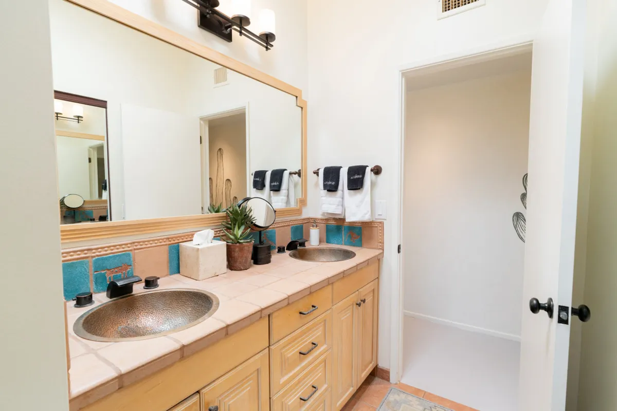 A spacious bathroom with dual sinks, stylish mirrors, decorative tiles, and a lush houseplant. The clean, refreshing space invites guests to enjoy peaceful self-care routines in a spa-like environment.