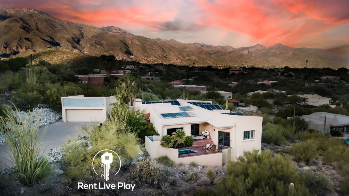 The hero image showcases a tranquil outdoor space with beautifully landscaped gardens, a modern single-family house featuring solar panels, and breathtaking views of the surrounding Tucson mountains at sunset. The inviting patio hints at relaxing evenings under the stars, perfect for gatherings or quiet reflection.