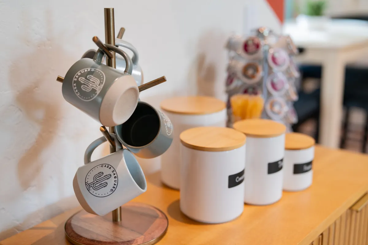 A cozy kitchen vignette with a mug stand, coffee canisters, and decorative elements, implying a dedicated coffee station. The setting is warm and welcoming, perfect for enjoying a French press brew.