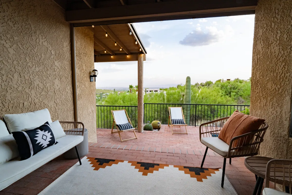 This exterior shot captures a comfortable outdoor seating area framed by cacti and desert greenery, oriented towards wide-open views of the landscape. The setting is calm and relaxed, suggesting both daytime and evening enjoyment, including sunset views and stargazing.