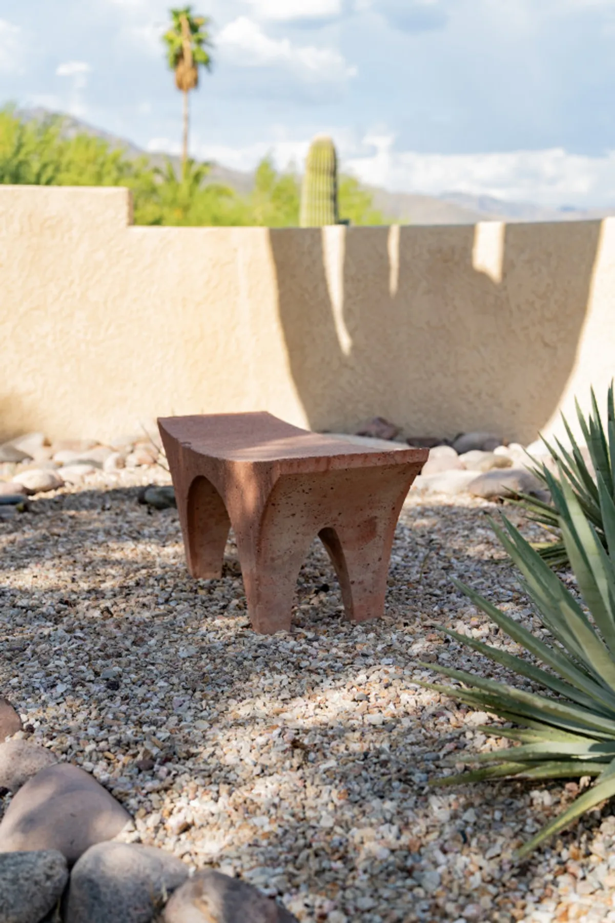 A ceramic bench sits in a tranquil desert garden, surrounded by cacti and gravel, with a wide view of the landscape. The scene evokes calm and invites moments of contemplation or casual socializing.