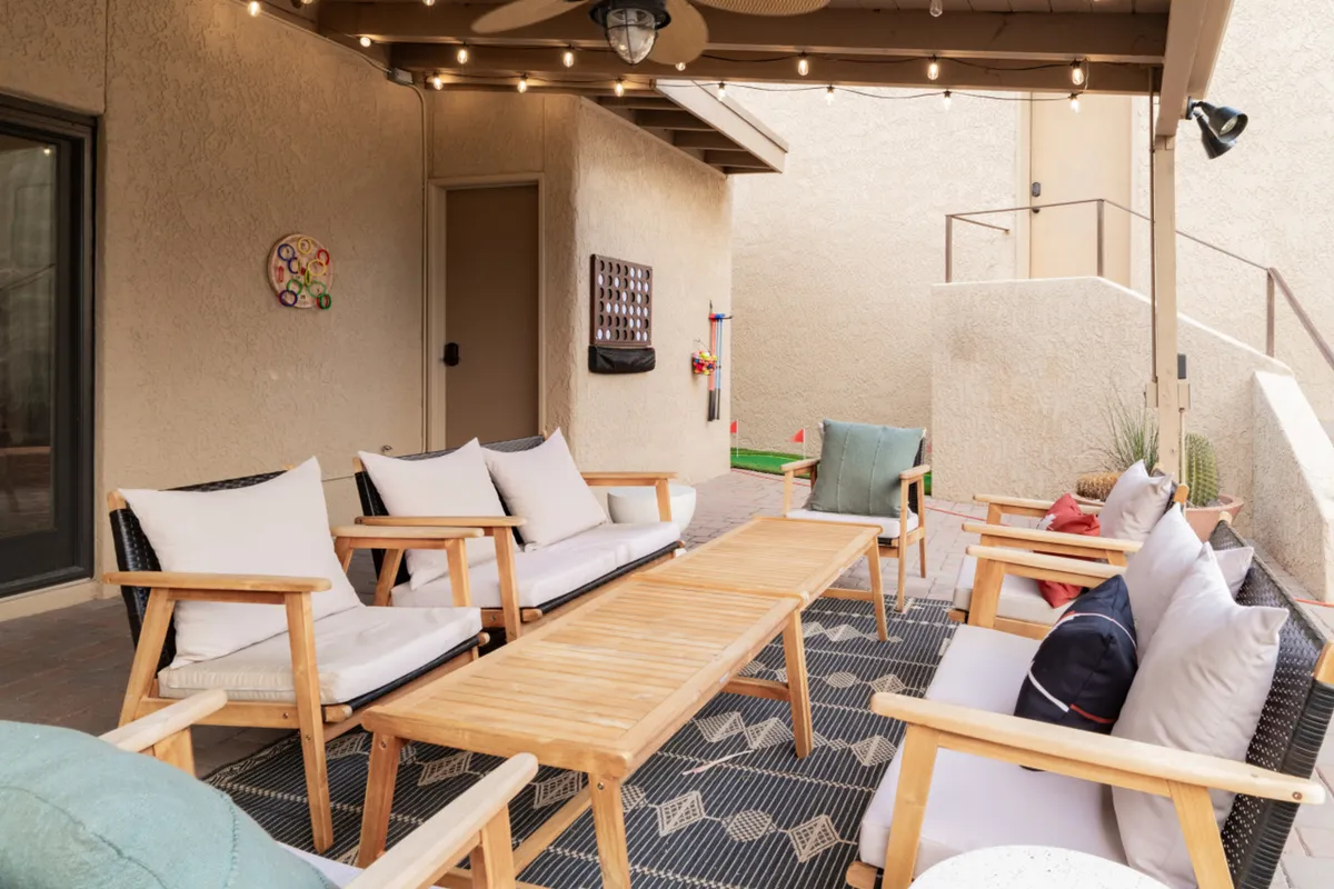 A cozy outdoor seating area featuring a wooden table and plush cushioned chairs with decorative pillows. The setup encourages socializing, outdoor dining, or unwinding in a casual, welcoming atmosphere. The covered patio environment alludes to sheltered comfort and protected privacy, ideal for families or pet owners.