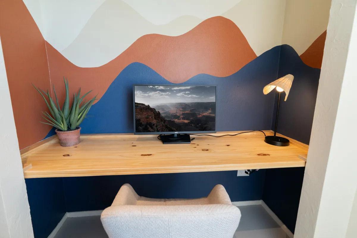A dedicated home office featuring a wooden desk with a monitor displaying a scenic landscape, a decorative lamp, and a potted plant. Natural accents and a tidy workspace create an inspiring and productivity-focused atmosphere.